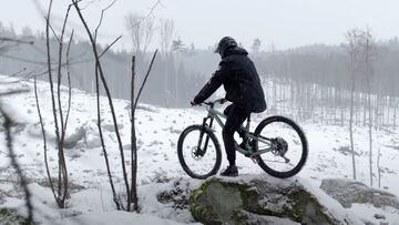 El rider Domink Pufer posando con su bici de mountain bike sobre una roca, rodeado de nieve. 