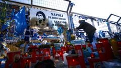 (FILES) In this file photo taken on November 26, 2020 A man attaches a scarf at a makeshift altar dedicated to the memory of late Argentinian football legend Diego Maradona, next to a board rechristening the stadium to &quot;Diego Armando Maradona stadium&quot;, as people gather on November 26, 2020 outside the San Paolo stadium in Naples to mourn the death of Maradona. - A resolution proposed by Naples&#039; Mayor Luigi de Magistris to rename the San paolo stadium after Diego Armando Maradona was approved by the municipal council on December 4, 2020. (Photo by Filippo MONTEFORTE / AFP)