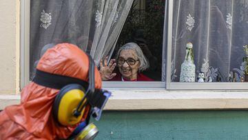 A woman waves to a city worker dressed in a hazmat suit as he disinfects the streets in her neighborhood as a precaution against the spread of the new coronavirus, in Santiago, Chile, Wednesday, April 15, 2020. (AP Photo/Esteban Felix)