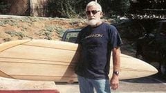 Pat Curren con una tabla de surf para olas grandes, gafas de sol, barba blanca... en un parking. 
