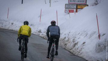 Varios ciclistas realizan la subida a Alpe d&#039;Huez entre paredes de nieve a los lados de la carretera.