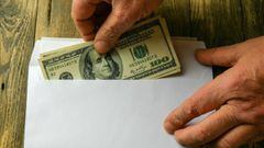 Persona metiendo dinero a un sobre v&iacute;a Getty Images.