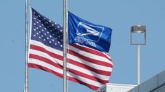 An American flag and US Postal service flag fly at half mast at a facility in Chelsea on August 17, 2020 in New York. - The United States Postal Service is popularly known for delivering mail despite snow, rain or heat, but it faces a new foe in President