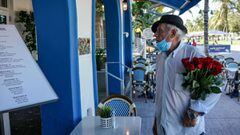 (FILES) In this file photo taken on June 09, 202, an elderly man holds a bouquet of roses as he looks at the menu outside a restaurant on Ocean Drive in South Beach, Miami. - More than a dozen US states are reporting their highest daily tolls of coronavir