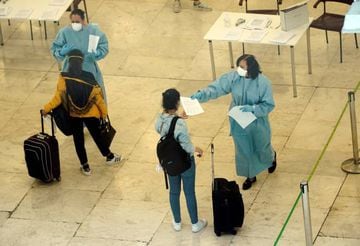 A healthcare worker wearing protective garments gives a passenger a document at the Adolfo Suarez Barajas Airport, after the Spanish government announced that from 15 May all people entering the country will have to go under quarantine for two weeks.