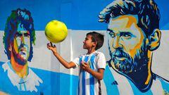 Un niño vestido con la camiseta de Argentina juega con una pelota frente a un mural en Bangladesh de las grandes leyendas de la selección albiceleste, Diego Armando Maradona y Lionel Messi, mientras los aficionados celebraban la victoria en las semifinales del Mundial de Qatar contra Croacia. 
