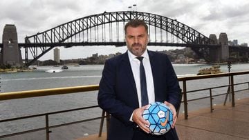 Australia&#039;s football coach Ange Postecoglou holds a football as he poses for a photo in front of the Sydney Harbour Bridge on September 27, 2017. Injured captain Mile Jedinak was on September 27 ruled out of Australia&#039;s crunch World Cup play-of