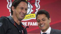 El delantero mexicano sonr&iacute;e junto al entrenador del Bayern Leverkusen, Roger Schmidt, durante una rueda de prensa en el BayArena en Leverkusen. 