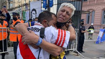 Soccer fans of rival soccer teams Boca Juniors, right, and River Plate, left, embrace as they wait to enter the presidential palace to see Diego Maradona lying in state in Buenos Aires, Argentina, Thursday, Nov. 26, 2020. The Argentine soccer great who led his country to the 1986 World Cup title died Wednesday at the age of 60. (AP Photo/Debora Rey)
