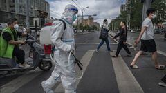 BEIJING, CHINA - MAY 13: A worker wears a protective suit as he crosses an intersection while disinfecting the area outside a nucleic acid testing site for COVID-19 on May 13, 2022 in Beijing, China. China is trying to contain a spike in coronavirus cases