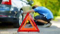 Red warning triangle sign on the road with a man checking his broken car in background