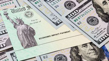 Cheque del departamento del Tesoro de Estados Unidos acompa&ntilde;ado de billetes de cien d&oacute;lares.