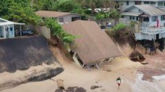 Una casa colapsa en la playa de Rocky Point, en el North Shore de Oahu (Haw&aacute;i, Estados Unidos), mientras un surfista pasa por delante, el 28 de febrero del 2022. 