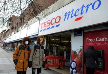A person wearing a face mask as a precautionary measure against COVID-19, walks past a Tesco supermarket store in north London.