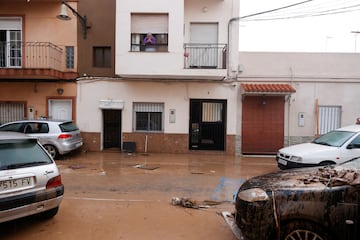 Una mujer mira por una ventana hacia una calle cubierta de barro después de que las lluvias torrenciales provocaran inundaciones en La Alcudia, región de Valencia.