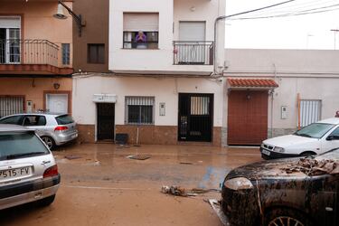 Una mujer mira por una ventana hacia una calle cubierta de barro después de que las lluvias torrenciales provocaran inundaciones en La Alcudia, región de Valencia.