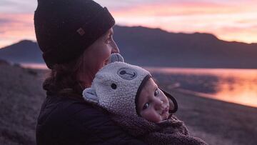 Kimmy Fasani con su hijo Koa, vestidos con gorros de invierno, mirando una puesta de sol en un lago. 