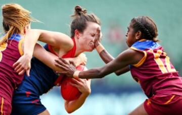 Daisy Pearce de los Melbourne Demons es bloqueada por Emily Bates y Delma Gisu de los Brisbane Lions en el partido de fútbol australiano femenino.