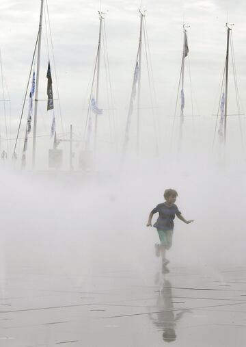 Un niño corriendo con las banderas ondeando en los mástiles de los barcos  antes de la salida de la 48ª Solitario-Le Figaro  en Burdeos