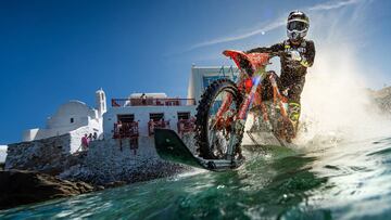 Robbie Maddison pilotando su moto por las aguas de Mykonos con las casas de la famosa isla de Grecia al fondo.