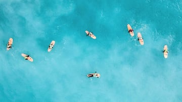 Varios surfistas principiantes esperan las olas en el lineup de uno de los picos de Razo, una de las mejores playas de España para aprender surf. El agua, color turquesa, las tablas, color naranja. Captados desde un dron.