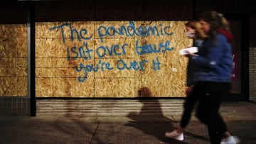 Women, one with and one without a protective mask, walk past graffiti on a boarded-up storefront reading &quot;The pandemic isn?t over because you&#039;re over it&quot;, amidst the coronavirus disease (COVID-19) in Madison, Wisconsin, U.S., October 17, 20