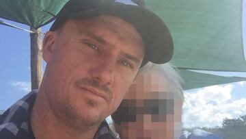 El surfista Chris Davidson, con gorra y camisa de cuadros, se hace un selfie acompañado de una mujer bajo un toldo verde.