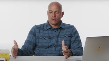 El 11 veces campe&oacute;n del mundo de surf, en camisa azul, sentado en una mesa con un mac y cera, gesticulando con las manos. 