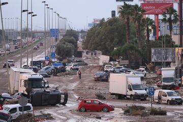 La gente camina junto a los automóviles y camiones que se encontraban entre los escombros arrastrados por las recientes inundaciones repentinas a lo largo de la carretera V-31 cerca del municipio de Massanassa el 1 de noviembre de 2024 en las afueras de Valencia, España.