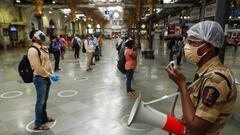 A railway police official makes an announcement on a loudspeaker telling commuters to stand inside the designated circles to maintain social distancing as they wait to board a train at a railway station after some restrictions were lifted during a lockdow