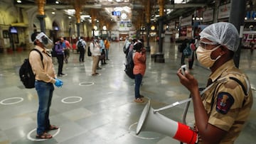 A railway police official makes an announcement on a loudspeaker telling commuters to stand inside the designated circles to maintain social distancing as they wait to board a train at a railway station after some restrictions were lifted during a lockdow