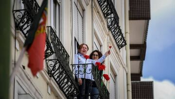 People hold up red carnations (symbol of the 25 April 1974 Portuguese Revolution) as they sing the Portuguese revolution anthem 'Grandola Vila Morena' marking 46th anniversary of 25th April Revolution at Graca neighborhood in Lisbon on April 25, 2020. - In the early morning of April 25, 1974, 'Grandola Vila Morena' by Portuguese singer-songwriter Zeca Afonso, was broadcasted on a Portuguese Catholic radio station, to signal the revolution kickoff, eventually becoming a symbol of the revolution and democracy in Portugal. The Portuguese celebrated the 46th anniversary of the Carnation Revolution today by singing at their windows, thereby circumventing the ban on gathering for traditional popular parades due to the coronavirus pandemic. (Photo by PATRICIA DE MELO MOREIRA / AFP)