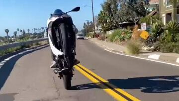 El Jackass del surf, Poopies, realizando un wheelie en moto por una carretera abierta al tráfico.