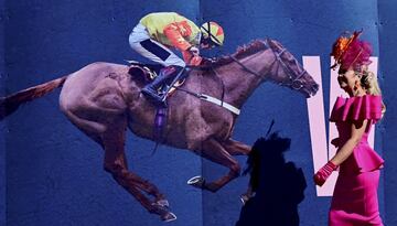 El hip¨®dromo de Aintree, en Liverpool, celebr¨® el D¨ªa de las Damas, durante la segunda jornada del Grand National Festival, la carrera de caballos de obst¨¢culos m¨¢s importante de las que tienen lugar en Reino Unido. En la imagen, una mujer pasa junto a un cartel ecuestre con un elegante vestido y un pomposo sombrero.