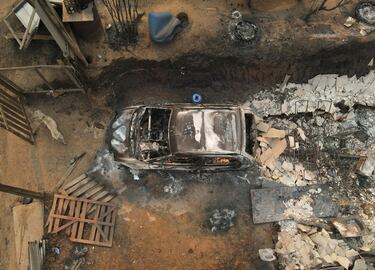 Un perro se encuentra junto a un automóvil quemado y los escombros de una casa.