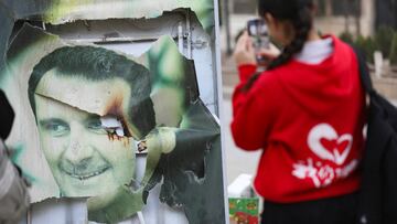 A woman uses her mobile phone near a damaged picture of Syrian President Bashar al-Assad as people celebrate, after Syrian rebels announced that they have ousted President Bashar al-Assad, in Qamishli, Syria December 8, 2024. REUTERS/Orhan Qereman