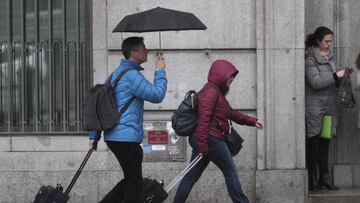Archivo - Dos turistas se refugian de la lluvia con paraguas, en Madrid (Espa&ntilde;a).