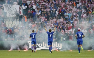 Croatia players gesture towards their fans as flares lie on the pitch.