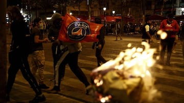 Paris Saint-Germain (PSG) supporters wave a PSG flag as they walk past a burning trash bin on the Champs-Elysees in Paris on August 23, 2020, after the end of the UEFA Champions League final football match against Bayern Munich at the Luz stadium in Lisbo