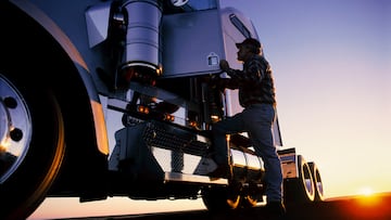 A silhouette of a truck driver getting into the cab of his commercial Class 8 truck tractor at sunrise.