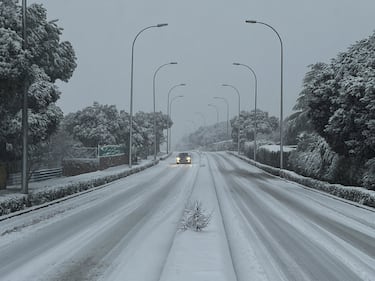 Un coche trata de seguir su camino en una carretera nevada en  Galapagar, municipio de la sierra madrileña.