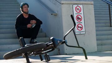El rider de BMX Dennis Enarson sentado en unas escaleras donde hay unas señales de prohibido ir en bici y patinar, con la bici en primer plano.