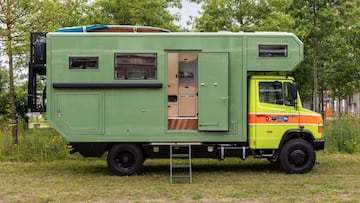 Exterior de una Mercedes Vario 4x4 que era un camión de bomberos suizo convertida en furgoneta camperizada o autocaravana, con una tabla de surf en el techo. De color verde.