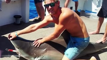 Aaron Moir, The Shark Rider (Jinete de tiburones), posando en ba&ntilde;ador sobre un tibur&oacute;n muerto, abriendo la boca. 