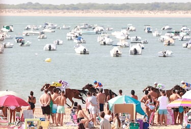 Un grupo de bañistas observa con atención una de las tradicionales carreras de caballos que tienen lugar cada verano en la playa de Sanlúcar de Barrameda (Cádiz), junto al Coto de Doñana. En este caso, es la primera jornada del segundo ciclo de carreras, que se celebran en la playa de Las Piletas y que finalizan el 30 de agosto.
