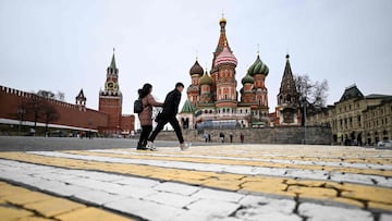 A couple walk in front of the Kremlin's Spasskaya tower and St Basil's cathedral in downtown Moscow on April 17, 2022. (Photo by Kirill KUDRYAVTSEV / AFP)