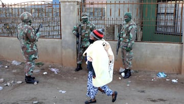A woman walks past members of the military during a protest by taxi operators over the government's financial relief for the taxi industry during the coronavirus lockdown in Soweto.