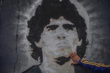 FILED - 25 November 2020, Argentina, Buenos Aires: A fan of the football club Boca Juniors puts his hand on a mural with the picture of the football star Diego Maradona on the day of his death.