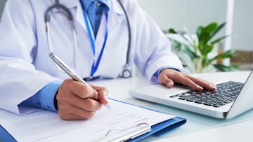 Doctor checking information in computer program before filling medical card