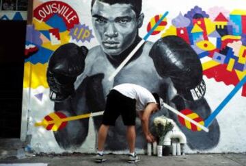 Un hombre deposita unas velas en un mural de Muhammad Ali  en Nueva York.